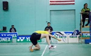 Badminton player lunges for shuttle and is on her knees.